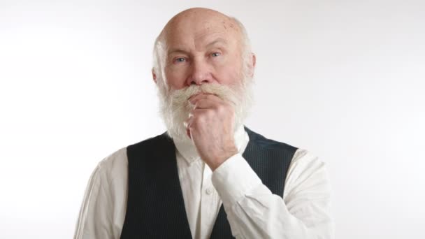 白いひげを持つ高齢者は シュートジェスチャーを作る 唇に指 正式な服装で 白い背景に立っています カメラ Raw — ストック動画