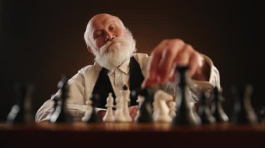 Yaşlı bir adam düşünce içinde sakalını okşar, sonra stratejik olarak atını hareket ettirir, rakip şövalyeyi yakalar, ve bir sonraki hamle için davetkar hareketler yapar. Kamera 8K HAM. 