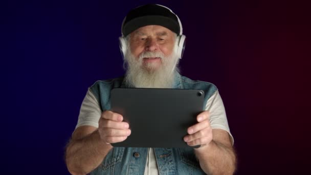 Hombre Mayor Que Usa Auriculares Involucra Alegremente Con Juego Tableta — Vídeos de Stock