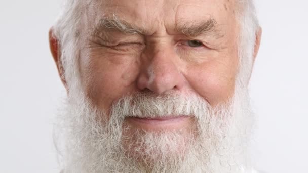 完全な白いひげを有する年配の男性は 一つの目と微笑みを遊んで きれいな白い背景に設定し スパイラルで柔らかいキャラクターを示しています カメラ Raw — ストック動画