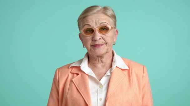 高傲的老妇人 金发碧眼 穿着白衬衫 站在橙色夹克 看着相机 卷曲着的嘴唇 有消化的 水蓝调的背景 工作室 高质量的4K镜头 — 图库视频影像