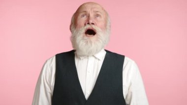 Yaşlı bir adam hapşırır ve sonra gülümsemeye başlar, bu da eylemden sonra rahatladığını gösterir. Onun giysisi ve yumuşak pembe arka planı sahneye rahat ve sade bir hava katıyor. Kamera 8K HAM. 