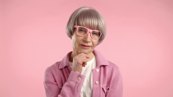 65歳以上のシニアレディは ピンクの背景と統一されたマッチングメガネのピンクのアンサンブルで ノードとの合意を表しています カメラ Raw — ストック動画