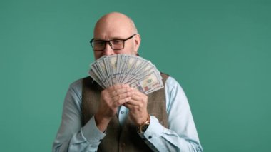Yelek giymiş yaşlı bir işadamı para hayranı, servetini ve finansal başarısını yatıştırıcı yeşil bir zemine karşı sergiliyor. Yüksek kalite 4k görüntü