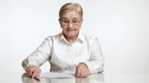 穿着白衬衫的金发老妇人坐在白桌旁 用铅笔写着白底 绝望地揉碎了一张纸 扔掉了 高质量的4K镜头 — 图库视频影像