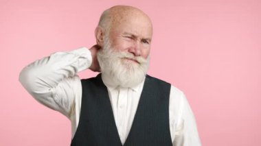 70 'li yaşlarının ortasında gibi görünen yaşlı bir adam nazikçe boynuna dokunuyor ve narin pembe bir arka planda kas gerginliği ya da rahatsızlık belirtileri gösteriyor. Kamera 8K HAM. 