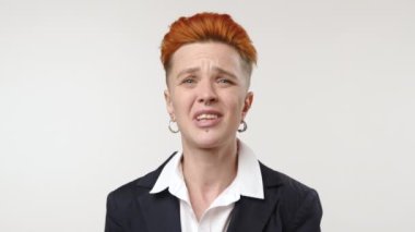 Canlı kızıl saçlı genç bir kadın beyaz bir arka plana karşı duruyor, net bir anlaşmazlık ya da reddetme jesti olarak kafasını sallıyor. Kamera 8K HAM.