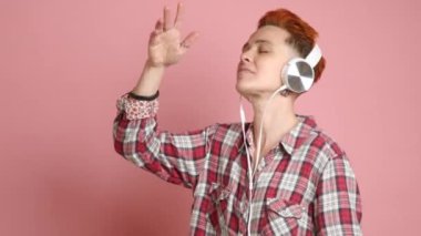 Huzurlu kızıl saçlı bir kadın, beyaz kulaklıklarla müzik dinlerken zevk alırken kayboldu, yumuşak pembe arka planda bir rahatlama havası uyandırdı. Yüksek kalite 4k görüntü