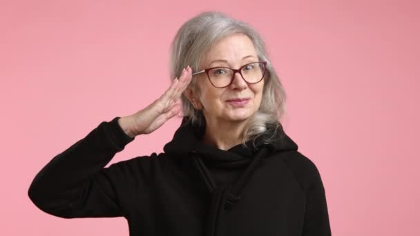 Zabawnym Salucie Wojskowym Radosna Starsza Kobieta Wyróżnia Się Różowym Tle — Wideo stockowe