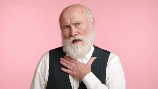 75歳の男性は 白いシャツと黒いベストの咳で 胸を優しいピンクの背景に対して抱きしめながら 不快感を表現しています カメラ Raw — ストック動画