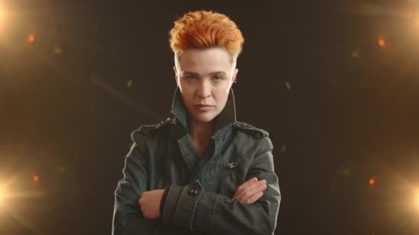 独特なオレンジ色の髪と顔のピアスを持つスタイリッシュなレズビアンロッカーは 暗い背景に明るいライトで照らされたカメラに深刻で強烈な外観を与えます カメラ Raw — ストック動画