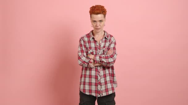 明るい赤い髪の若いレズビアン チェッカーされた平らなシャツは 柔らかいピンクの背景に立って陽気なポーズを提供しています カメラ Raw — ストック動画