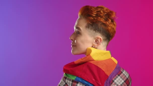 一位年轻的女同性恋者转身面对镜头 在一个动态的粉色和紫色渐变背景下 展示着彩虹Lgbt旗 带着真实的笑容 8K照相机 — 图库视频影像