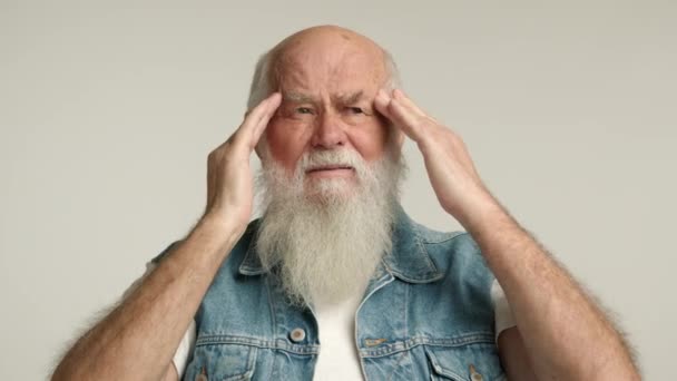 白いひげを持つ困窮した高齢者が重度の頭痛に苦しんでおり 寺院を平凡な背景に押しつけているようだ カメラ Raw — ストック動画