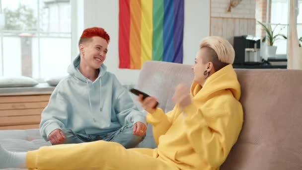 当一个女人把头靠在同性恋伴侣的膝上 两人都在欣赏电视节目时 一场亲密的场面展现了出来 在他们身后醒目地展示着一个充满活力的骄傲的旗帜 — 图库视频影像