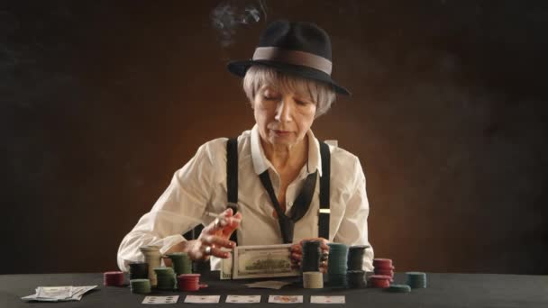 65歳の女性が暗い部屋で ギャングをタバコで見て 大胆にすべての現金をテーブルの上に置き ハイステークスポーカー賭けをします カメラ Raw — ストック動画