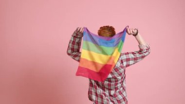 Neşeli bir lezbiyen kadın küçük bir LGBT bayrağı sallıyor, arkası dönük, kimliğindeki sevinç ve gururu simgeliyor. Yüksek kalite 4k görüntü