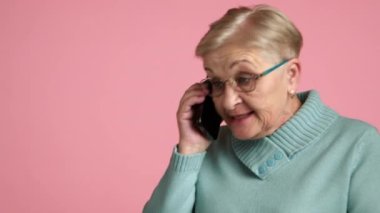 Yaşlı, bakımlı, kısa saçlı, fevri, gözlüklü, mavi kazaklı bir kadın cep telefonunda tatsız bir konuşma yapıyor, gergin bir şekilde elini sallıyor. Yüksek kalite 4k görüntü