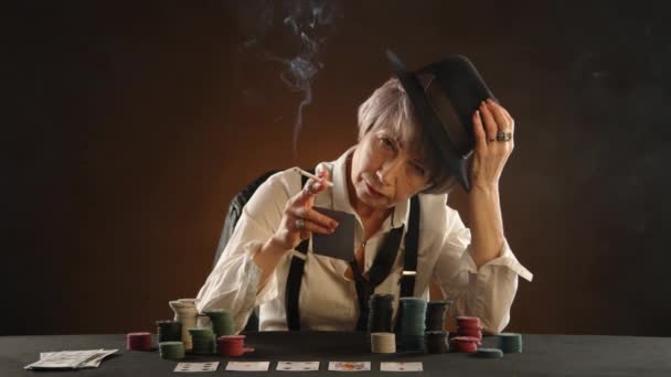 一位老练的老妇人 拿着一支香烟和一只获胜的扑克手坐在赌场桌旁 为自己的胜利感到自豪 8K照相机 — 图库视频影像