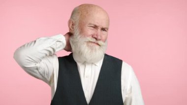 70 'li yaşlarının ortasında gibi görünen yaşlı bir adam nazikçe boynuna dokunuyor ve narin pembe bir arka planda kas gerginliği ya da rahatsızlık belirtileri gösteriyor. Kamera 8K HAM. 