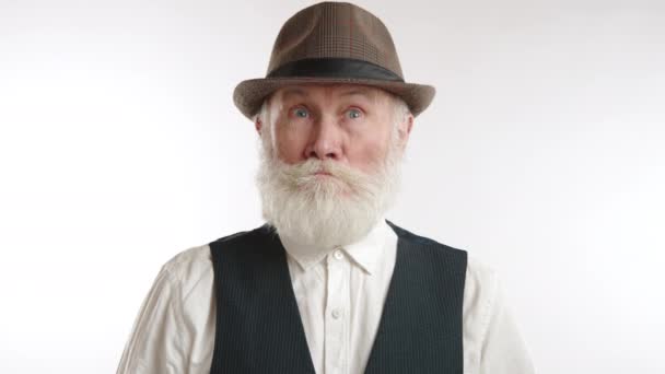 一位留着白胡子 头戴帽子的老年绅士 带着惊讶和惊讶的神色 面对着一副赤裸裸的白色背景 8K照相机 — 图库视频影像