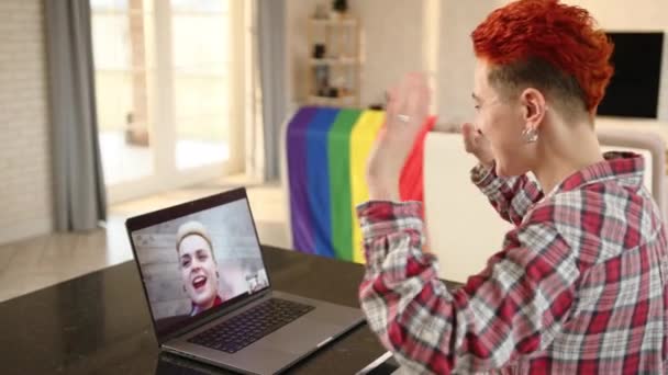 心からのバーチャルミーティングで ラップトップ画面のパートナーの鮮やかな赤いヘアカット波を持つ女性は バックグラウンドにLgbtフラグが付いた居心地の良い部屋でテクノロジーに架けられた接続 — ストック動画