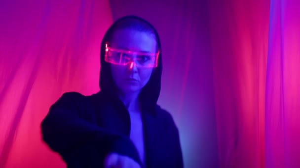 一位穿着黑色斗篷 戴着发光眼镜的网络朋克主题女性优雅地穿梭在布满红光的房间里飘扬的窗帘之间 高质量的4K镜头 — 图库视频影像