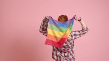 Neşeli bir lezbiyen kadın küçük bir LGBT bayrağı sallıyor, arkası dönük, kimliğindeki sevinç ve gururu simgeliyor. Yüksek kalite 4k görüntü