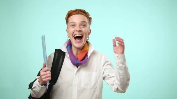 レズビアンの学生は タブレットを持ち バックパックを着て 柔らかい青い背景に対して笑いと喜びを伝えます 高品質の4K映像 — ストック動画
