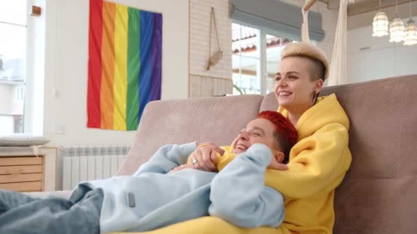 2人の愛する女性の間の居心地の良い抱擁は 明るいリビングルームのソファーでリラックスするので プライドの虹の旗は暖かく スペースを誘います カメラ Raw — ストック動画