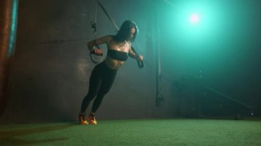 Avrupa görünümlü bir kızın ek ekipmanlarla bir spor salonunda fonksiyonel eğitim yaparken çekilmiş bir video montajı. Kız halterlerle ve vücut ağırlığıyla çalışıyor.
