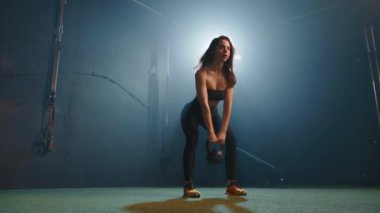 Dumanlı, soğuk ışıkta bir spor salonunda genç bir atletik kızın yakın plan ve geniş açılı çekimlerinin video montajı. Sonunda, kız şişeden su içiyor..