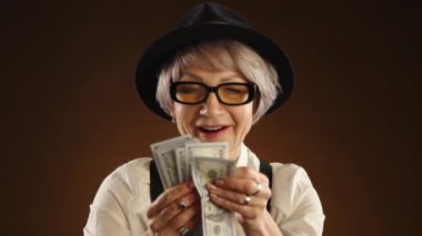 Yüzünde gülümseme olan yetişkin bir kadın zenginleşme anının tadını çıkararak büyük miktarda para sayıyor. Eski moda kıyafetler giymişti, şapka ve pantolon askısı da vardı. Kamera Ham 