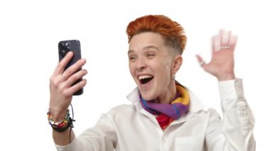 Renkli sporlara yeteneği olan keyifli bir LGBTQ şahsiyeti canlı bir video görüşmesinde gökkuşağı eşarbı ve kızıl saçlı, beyaz gömlekli, neşeleri beyaz arka planda bulaşıcı..