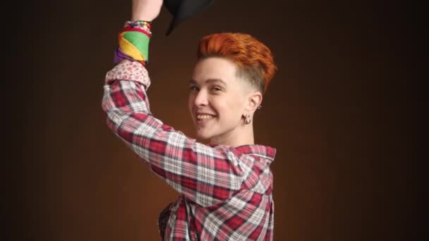 活気に満ちたオレンジ色の髪を持つレズビアンは プライドと多様性を象徴する黒い帽子を陽気に出し すべて暖かい茶色の背景に設定されています カメラ Raw — ストック動画