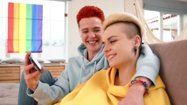 一对女同性恋夫妇舒适地坐在家里 笑着自豪地在手机上展示超声波图像 背景上挂着五彩缤纷的Lgbt旗 高质量的4K镜头 — 图库视频影像