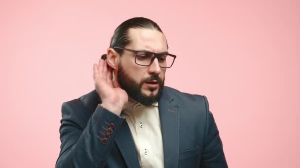 穿着合身西服 眼神专注的男人 做了一个耳朵对耳朵的手势 好像在偷听 背景是光滑的粉红的 在商业中积极聆听的象征 — 图库视频影像