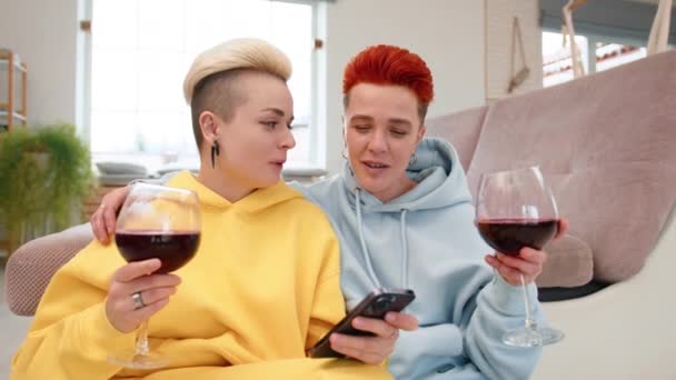 2人の女性は平和な瞬間を共有し ソファーに座って快適にワインを楽しんで 1人のパートナーは愛情を持って他の人に額にキスします 高品質の4K映像 — ストック動画