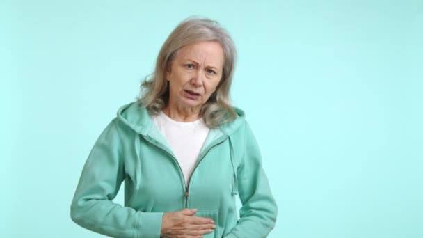 Пожилая Женщина Сжимает Живот Боли Носит Зеленую Толстовку Обеспокоенное Выражение — стоковое видео