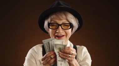 Yüzünde gülümseme olan yetişkin bir kadın zenginleşme anının tadını çıkararak büyük miktarda para sayıyor. Eski moda kıyafetler giymişti, şapka ve pantolon askısı da vardı. Kamera Ham 