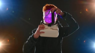 Genç bir kadın, sanal gerçeklik deneyimine dalmak isteyen, cihazın mavi ışığı olan VR gözlüklerini takarken heyecanlanıyor. Kamera 8K HAM. 