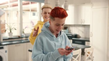 Evinde, sarı kapüşonlu bir kadının partnerine alyansla sürpriz yaptığı, neşeli bir reaksiyona ve lezbiyen çift arasında duygusal bir kucaklaşmaya yol açan samimi bir evlenme teklifi sahnesi.. 