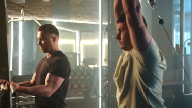 İyi donanımlı spor salonunda, iki odaklanmış adam aynı anda kollarını ve sırt kaslarını güçlendirmek için kablo çapraz makinesini kullanıyor, yoğun fitness rutinlerine daldırıyorlar. Kamera 8K HAM. 