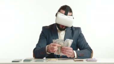 Sanal gerçeklik kulaklığı takan odaklanmış bir işadamı banknotlarla etkileşime giriyor ve beyaz arka planda modern finans teknolojisi olduğunu öne sürüyor. Kamera 8K HAM. 