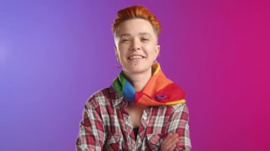 Boynunda LGBTQ gökkuşağı eşarbı olan neşeli lezbiyen kız canlı mor bir arka plana karşı mutlu bir şekilde poz veriyor. Etkileyici, olumlu ve renkli bir portre. Kamera 8K HAM. 