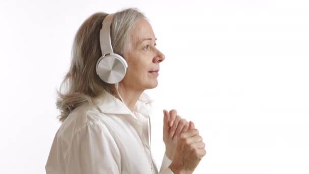 这张照片显示了一位年长的女性迷失在音乐节奏中 她通过耳机听着音乐 她的肢体语言表达着舞蹈的欢乐和音乐带来的自由 — 图库视频影像