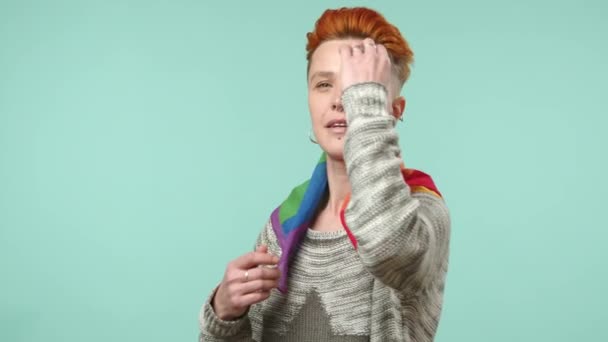 鮮やかな髪を持つレズビアンの女性は カメラのために陽気なポーズをし 誇りを象徴する虹のスカーフは パステルティールの背景に対して幸福を表します カメラ Raw — ストック動画