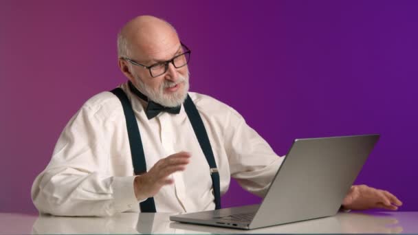 一位活跃的老人通过笔记本电脑上的视频通话进行了热烈的讨论 带着激情在紫色的背景下做了一个明确的手势 8K照相机 — 图库视频影像
