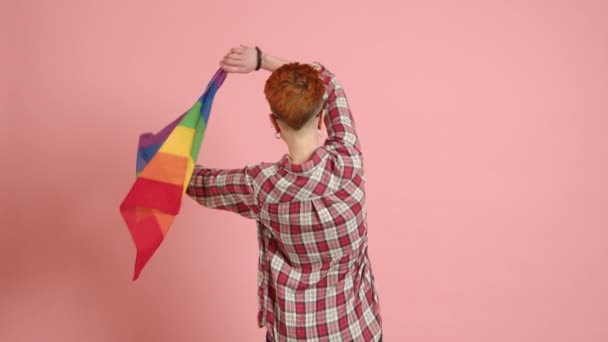 一位Lgbtq的倡导者背对着镜头站着 迅速地挥动着一个充满活力的彩虹旗 然后在粉色的背景下 面带微笑地转向镜头 8K照相机 — 图库视频影像