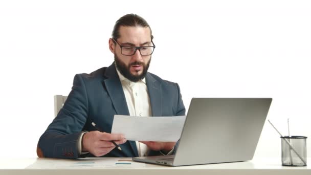 眼鏡に勤勉なビジネスマンは オフィスの設定で勤勉な仕事倫理を示す 彼のラップトップ上の文書を慎重にレビューしています カメラ Raw — ストック動画